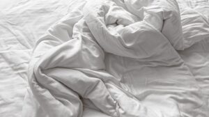 an unmade bed with white sheets and pillows